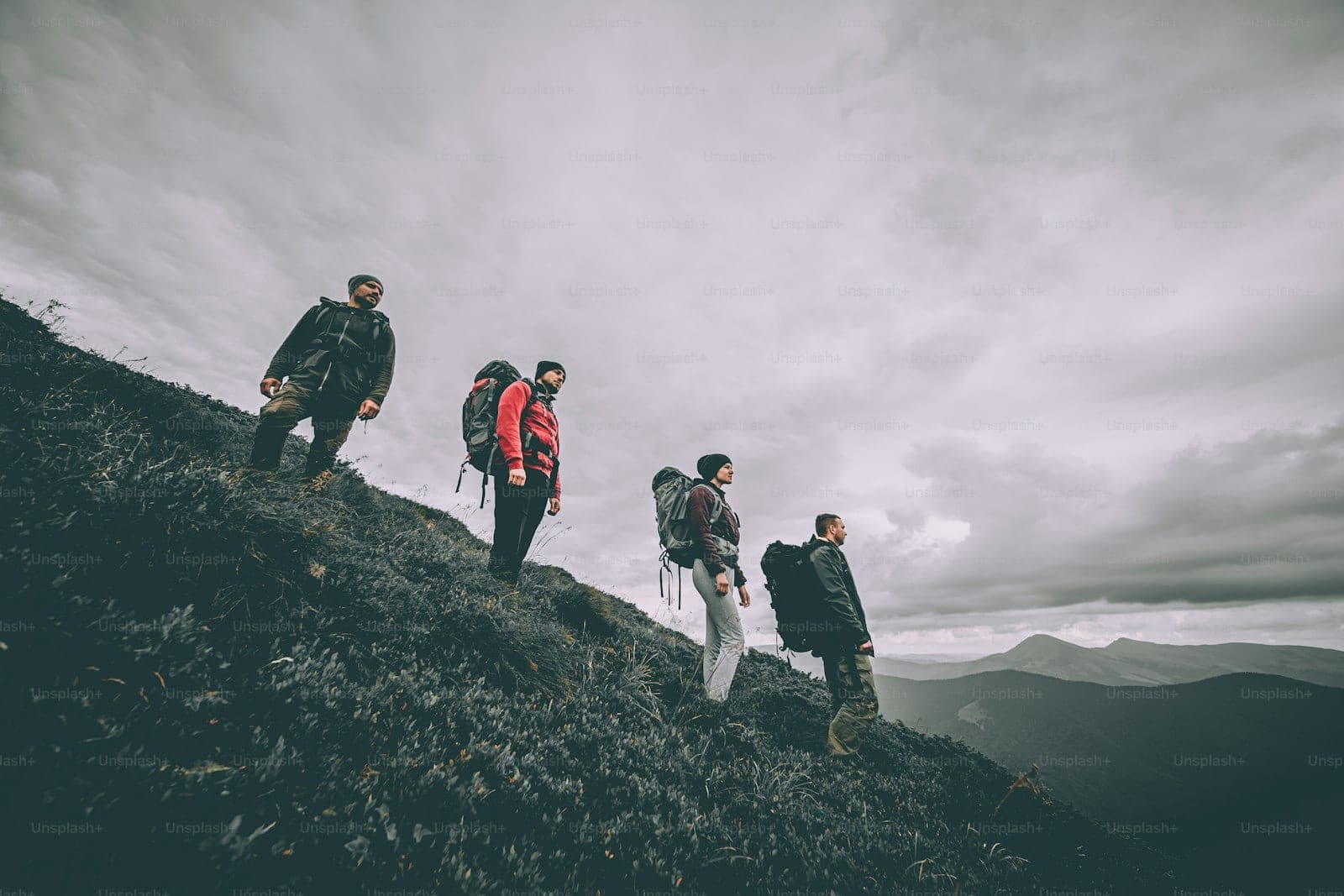 Four hikers standing on a mountain ridge under a cloudy sky