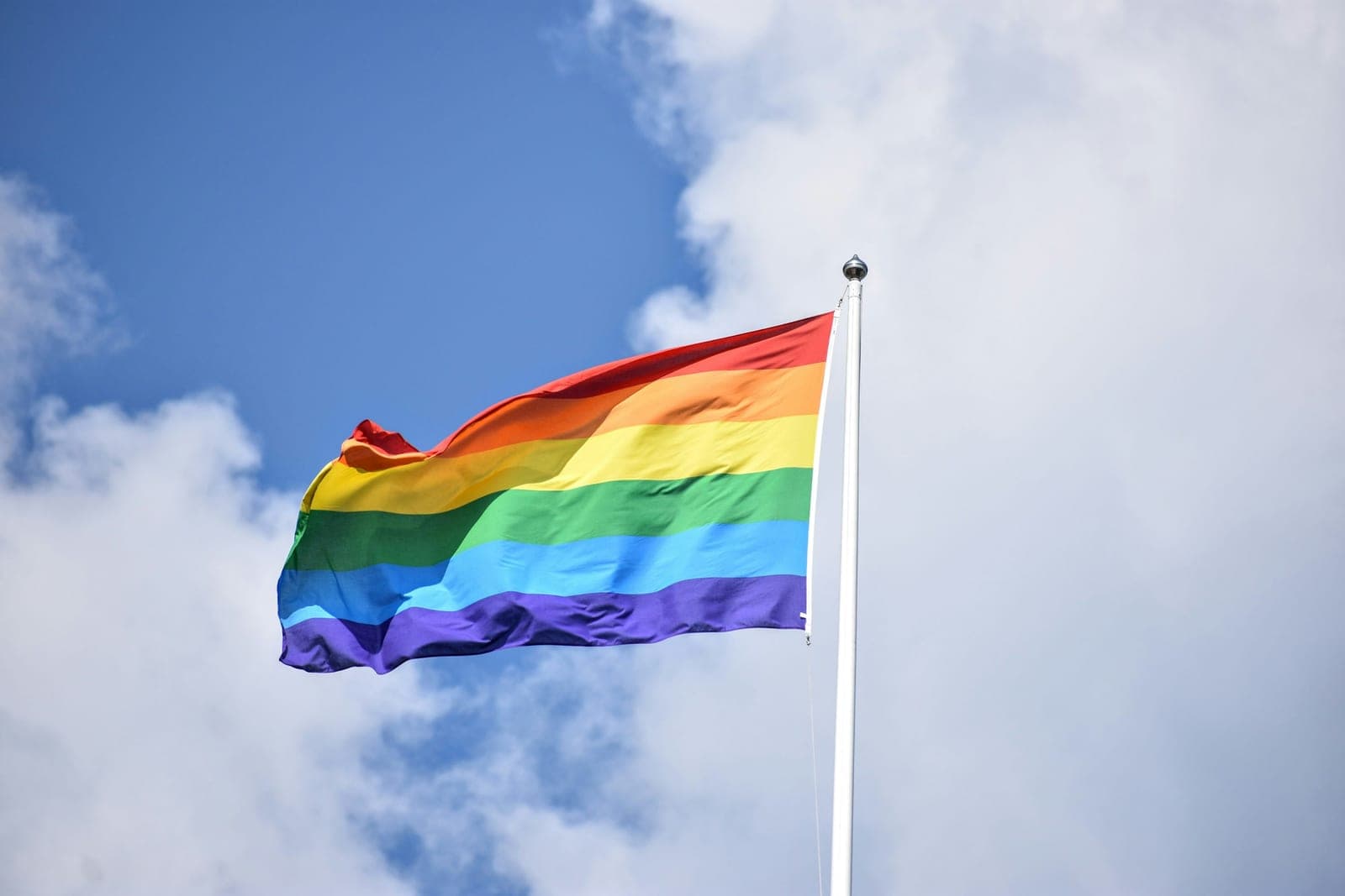 Rainbow pride flag flying high against a blue sky