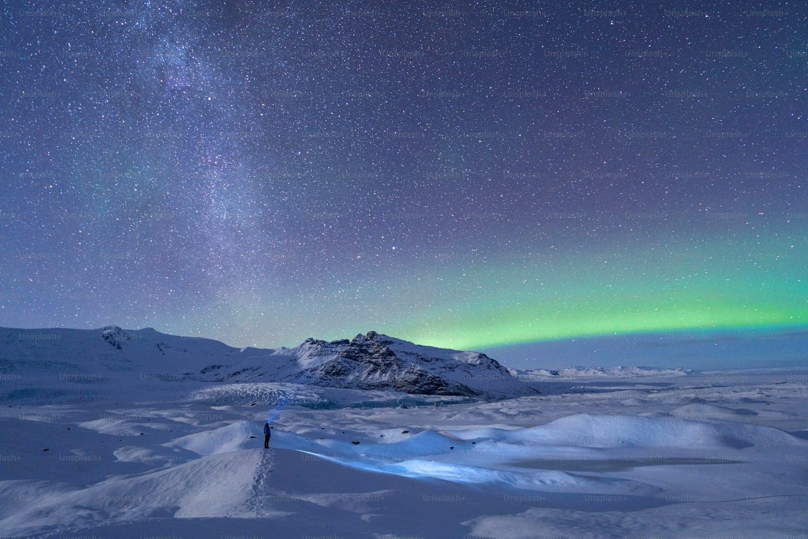 Snowy landscape under the northern lights and a star-filled sky