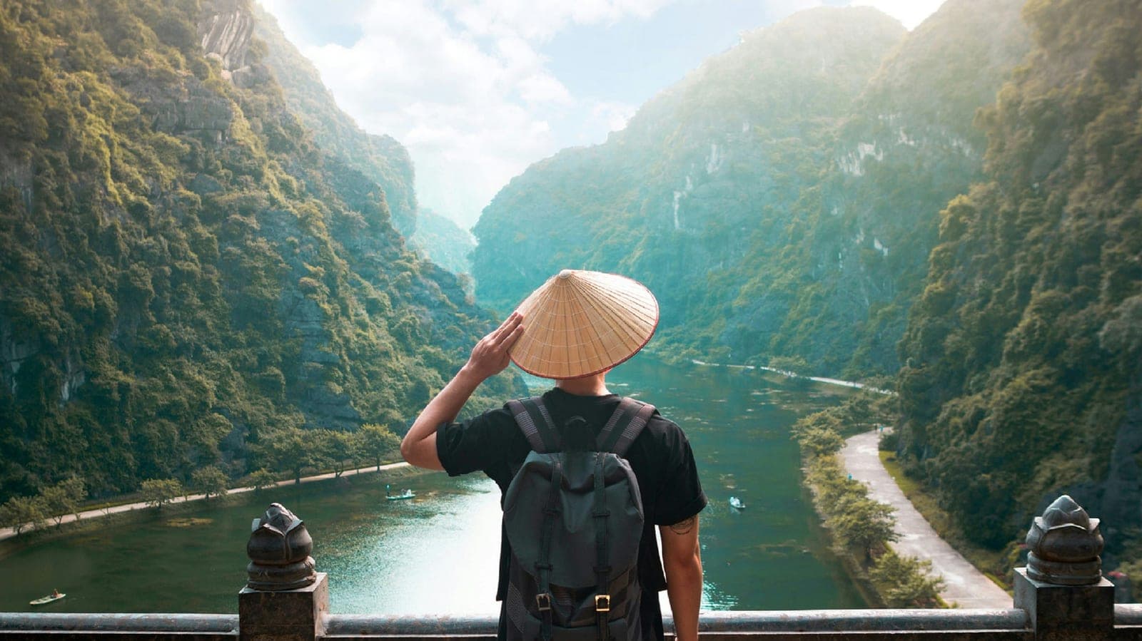 Traveler in a conical hat overlooking a river valley between karst cliffs