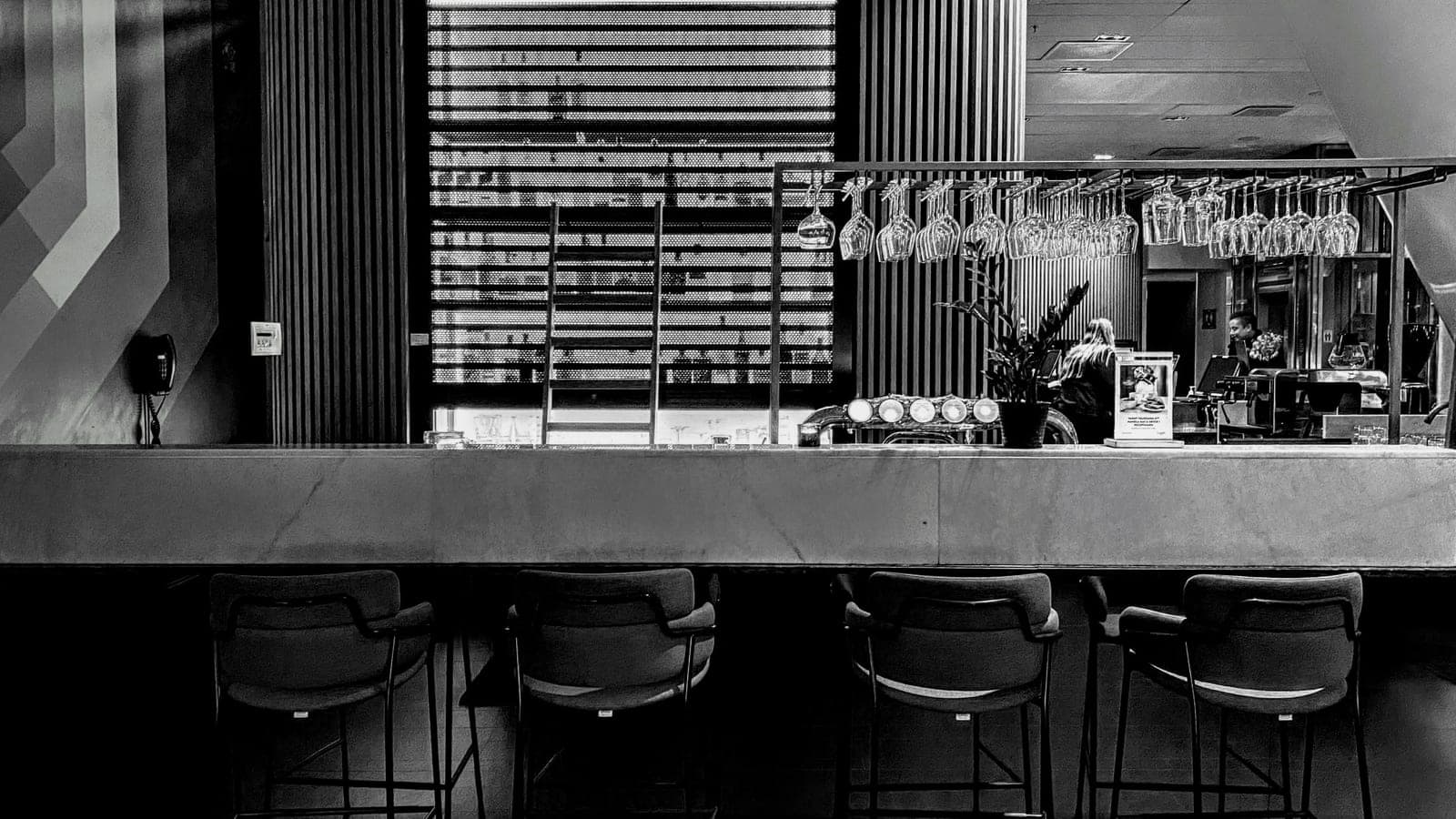 Black-and-white hotel bar interior with stools and hanging glasses